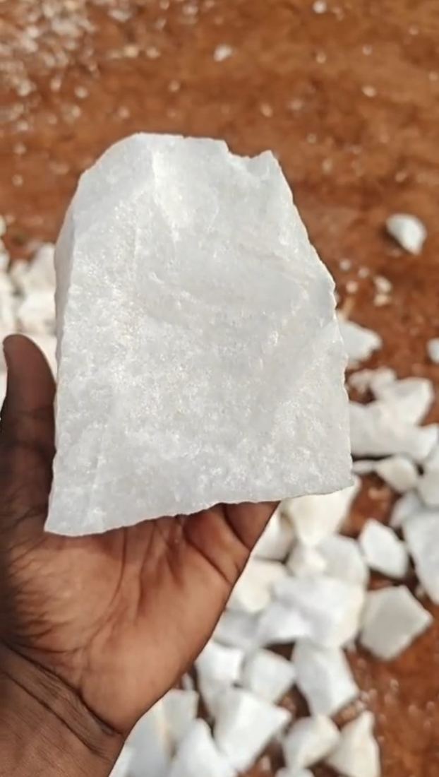 Hand holding a lump of white A-Grade quartz above red soil